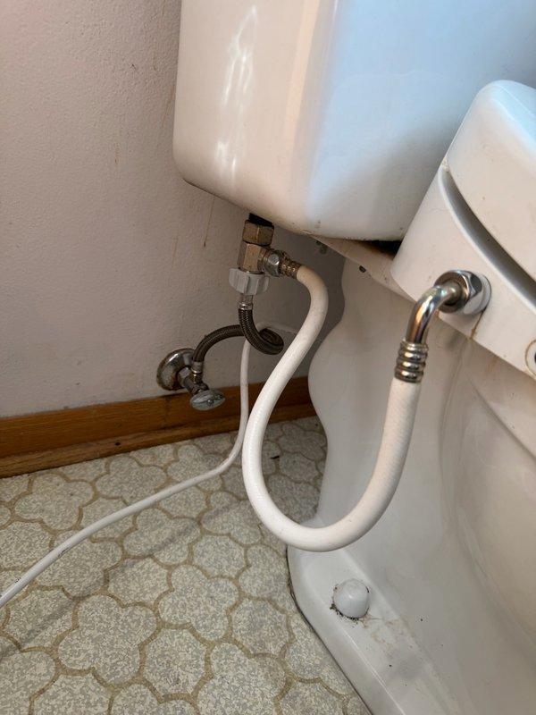 Responded to emergency plumbing call for toilet flooding issue caused by failed wax ring seal and defective water supply connections. Main water supply was shut off upon arrival due to uncontrollable flooding when turned on, as the toilet's individual shut-off valve was inoperable and missing its handle. Removed and reset toilet after discovering deteriorated wax ring causing leak at floor flange connection. Replaced old angle stop valve with new unit featuring proper shutoff handle for future maintenance access. Repaired compression fitting on water supply line and installed new braided stainless steel flexible supply line to ensure secure, leak-free connection between angle stop and toilet tank fill valve. Tested all connections under full water pressure to confirm proper operation and verified no leaks at wax ring seal, angle stop valve, or supply line connections.