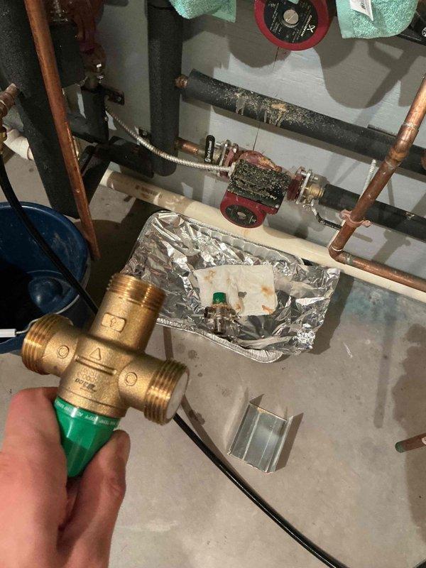 Removed existing mixing valve from water heating system and installed new brass mixing valve with coupling to properly regulate water temperature. System tested and verified operational with appropriate temperature control functionality restored.