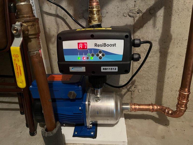 Responded to low water pressure complaint and diagnosed residential water pressure boosting system with ResiBoost variable frequency drive controller. Upon inspection, found controller had short circuited and displayed persistent error code A7 even after disconnecting pump and resetting unit. Tested system components and confirmed controller failure requiring replacement. Documented existing installation showing blue electric pump motor with metallic housing, copper piping connections, and failed ResiBoost control unit mounted on pump assembly. Photographed internal circuit board damage and wiring configuration for reference. Due to specialized nature of ResiBoost VFD programming and limited technician availability in the area for this equipment, provided estimate for new controller installation to restore proper water pressure boost functionality to the residential water system.