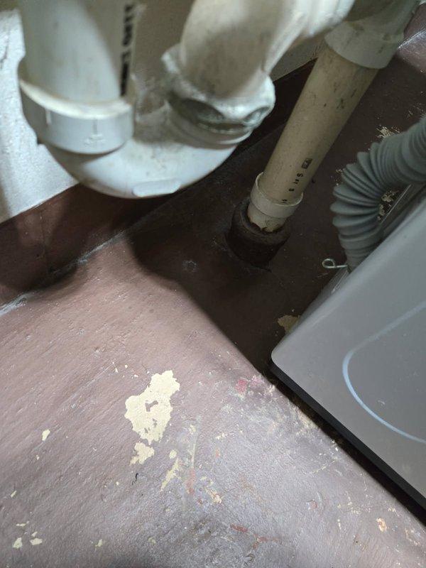 Responded to floor drain backup occurring during laundry operation. Attempted to clear blockage by snaking both the floor drain and the main stack line. Inspected laundry drain plumbing system including P-trap connections and drainage assembly beneath fixtures. Work performed in utility area with exposed plumbing infrastructure along cinder block walls.