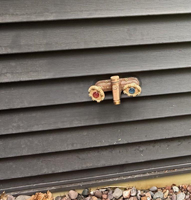 Returned to address misaligned valve handles on a recently installed dual-control outdoor faucet assembly. The hot and cold water handles were positioned at crooked angles when in the closed position due to a factory defect that was not identified during initial installation. Removed mounting screws from both handles and repositioned them to achieve proper alignment, ensuring both valve controls now sit at matching angles when shut off.
