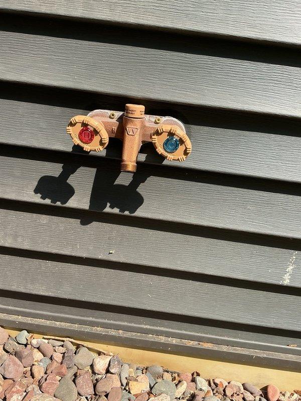 Returned to address misaligned valve handles on a recently installed dual-control outdoor faucet assembly. The hot and cold water handles were positioned at crooked angles when in the closed position due to a factory defect that was not identified during initial installation. Removed mounting screws from both handles and repositioned them to achieve proper alignment, ensuring both valve controls now sit at matching angles when shut off.