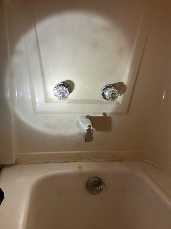 Responded to a water leak complaint originating from a tub faucet spraying behind the wall. Accessed the plumbing through an adjacent room opening, where inspection revealed significant water damage to the wooden back panel with extensive dark staining and moisture accumulation, indicating prolonged leakage from the deteriorated tub faucet assembly. The existing two-handle tub faucet without shower capability required replacement. Documented the condition of the plumbing installation, including corroded supply lines and damaged surrounding materials. Provided an estimate for replacing the widespread tub faucet and scheduled a follow-up appointment to present additional options for installing a complete tub and shower surround system with integrated showerhead functionality.