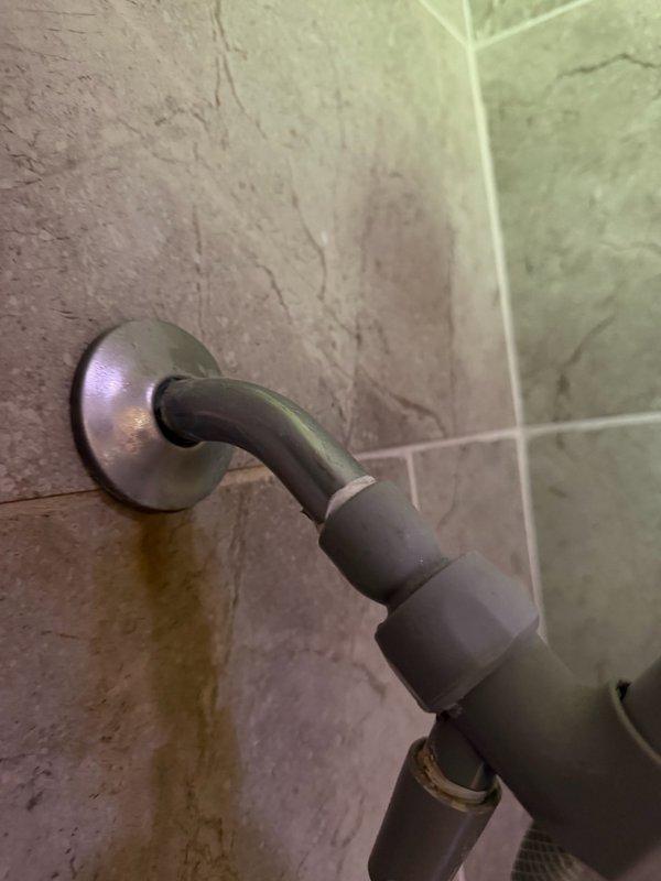 Responded to water leak originating from master bathroom shower affecting basement drop ceiling below. Upon investigation, identified shower head was spraying backwards toward wall, allowing water infiltration behind the escutcheon plate and subsequently running down interior drywall. Removed defective shower head and installed new replacement unit. Applied silicone sealant behind escutcheon to create proper water barrier and prevent future moisture penetration into wall cavity.