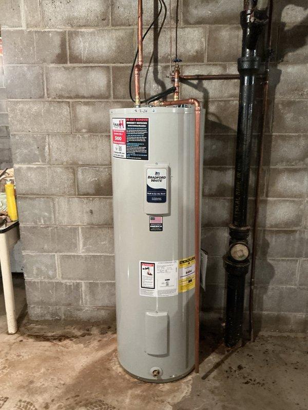 Responded to emergency call for water heater leaking from bottom and flooding basement. Upon arrival, found original unit installed in 1968, approximately 60 years old, actively leaking and causing water damage to basement floor. Assessed that tank had reached end of service life with catastrophic failure at base of unit. 

Shut off water supply and electrical power to failed water heater. Drained remaining water from old tank and disconnected all plumbing connections including cold water inlet and hot water outlet copper lines. Disconnected electrical wiring at junction box. Removed failed 50-gallon electric water heater from basement utility area and prepared installation site.

Installed new Bradford White 50-gallon electric water heater in same location against concrete block wall. Unit specifications include 240V operation with dual 4500W heating elements (upper and lower). Connected copper supply lines to top of new tank, ensuring proper hot and cold water line orientation. Recon