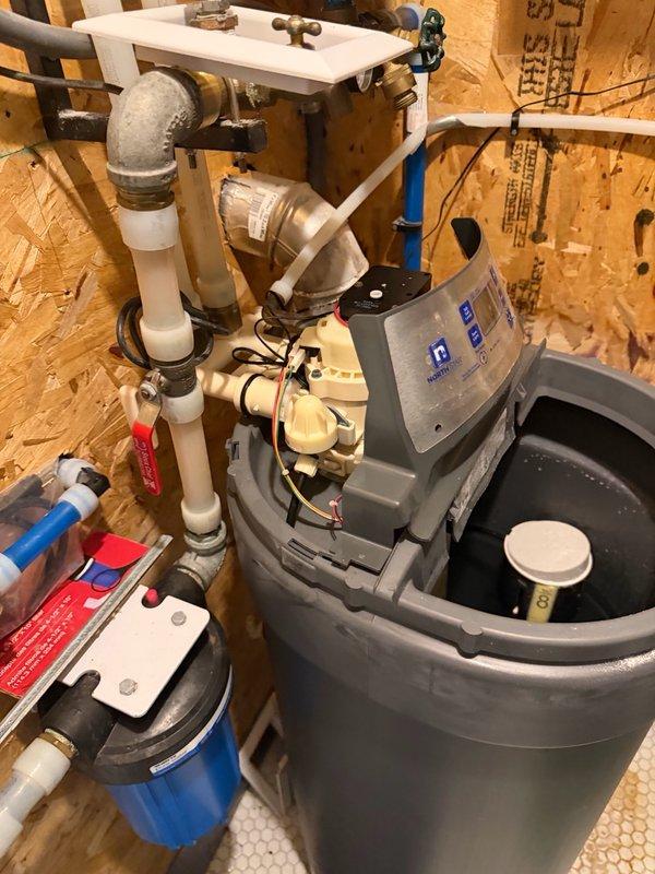 Responded to service call for water softener displaying ERR1 error code and failing to drain properly. Upon inspection, diagnosed 7-year-old unit with malfunctioning motor preventing water discharge through drain port during regeneration cycle. Motor mechanism not operating correctly, causing system to fill with water and halt regeneration process. Evaluated cycle controller assembly and drainage components to confirm motor failure as root cause. Documented equipment condition with photographs showing cycle controller, valve assembly, PVC plumbing connections, and complete water treatment system configuration including associated filtration components. Provided customer with multiple repair options including motor replacement, complete resin rebed service, or new water softener unit installation to restore proper system operation.