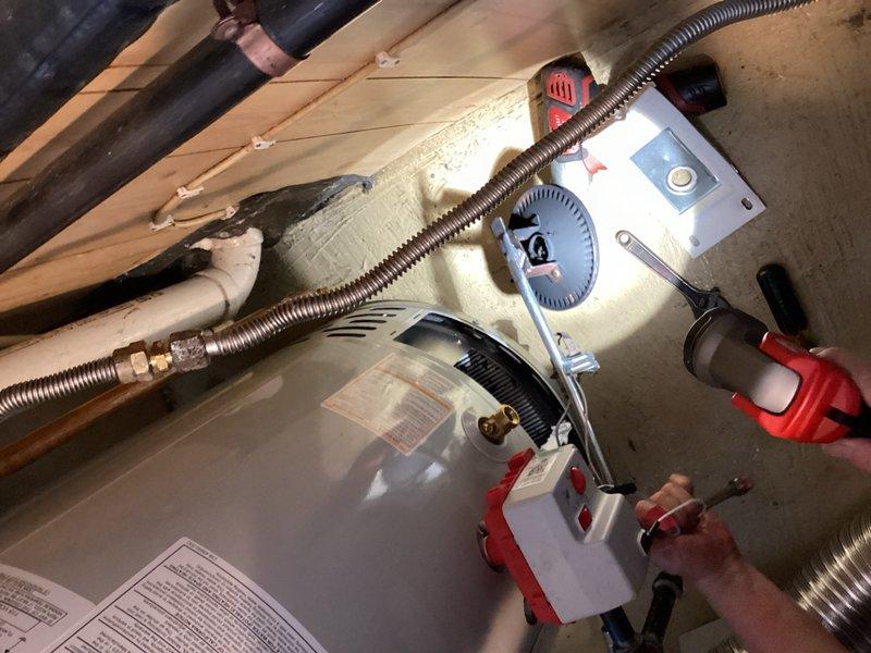 Responded to service call for pilot light relight following propane tank refill. Successfully relit both furnace and tanked water heater units. Upon inspection, discovered excessive soot buildup on water heater burner assembly indicating incomplete combustion. Performed comprehensive leak detection test on all gas fittings and connections throughout system using combustible gas detector—no leaks detected. Cleaned burner plate and combustion chamber of accumulated soot and debris. Water heater continued to exhibit rolling flame pattern after cleaning, indicating ongoing combustion efficiency issues likely caused by insufficient primary air intake or compromised burner orifice. Documented conditions with photos showing equipment setup, testing procedures, and current installation configuration in attic space. Unit operational but requires further evaluation and potential burner assembly replacement to resolve improper flame characteristics and prevent continued soot accumulation.
