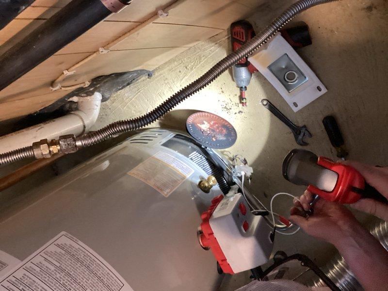 Responded to service call for pilot light relight following propane tank refill. Successfully relit both furnace and tanked water heater units. Upon inspection, discovered excessive soot buildup on water heater burner assembly indicating incomplete combustion. Performed comprehensive leak detection test on all gas fittings and connections throughout system using combustible gas detector—no leaks detected. Cleaned burner plate and combustion chamber of accumulated soot and debris. Water heater continued to exhibit rolling flame pattern after cleaning, indicating ongoing combustion efficiency issues likely caused by insufficient primary air intake or compromised burner orifice. Documented conditions with photos showing equipment setup, testing procedures, and current installation configuration in attic space. Unit operational but requires further evaluation and potential burner assembly replacement to resolve improper flame characteristics and prevent continued soot accumulation.