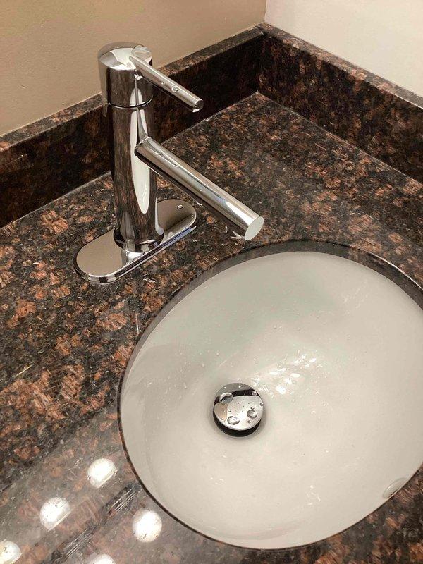 Installed two customer-supplied chrome bathroom faucets on undermount sinks with dark granite countertops in a single bathroom. During installation, identified a loose drain connection above the P-trap that required attention to ensure proper seal and prevent future leaks.