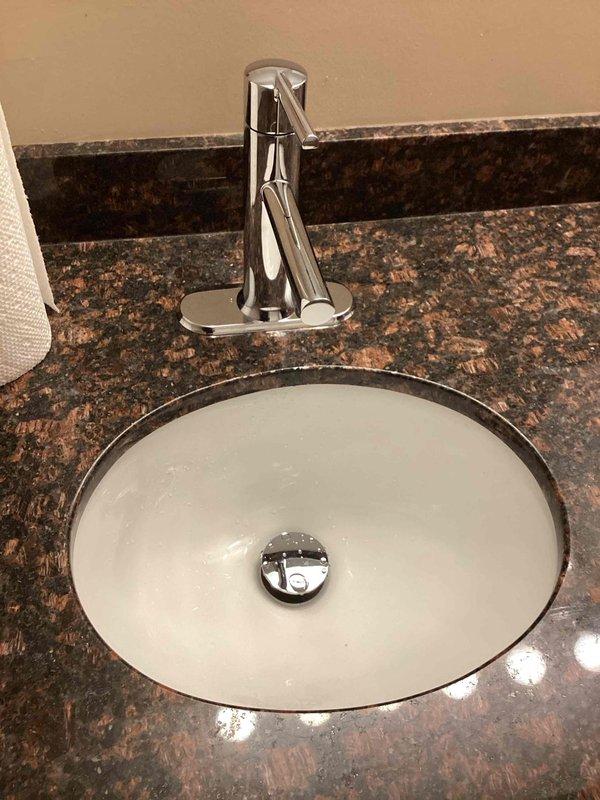 Installed two customer-supplied chrome bathroom faucets on undermount sinks with dark granite countertops in a single bathroom. During installation, identified a loose drain connection above the P-trap that required attention to ensure proper seal and prevent future leaks.