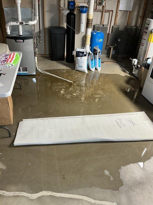Responded to emergency call for basement flooding caused by backed-up sewer system. Upon arrival, found standing water throughout basement utility room and discovered main sewer tank completely full of sewage and toilet paper. Accessed main line cleanout opening and assessed condition of system. Customer arranged for septic pumping service to address full tank. Documented conditions of flooded basement mechanical room and main line access point for records.