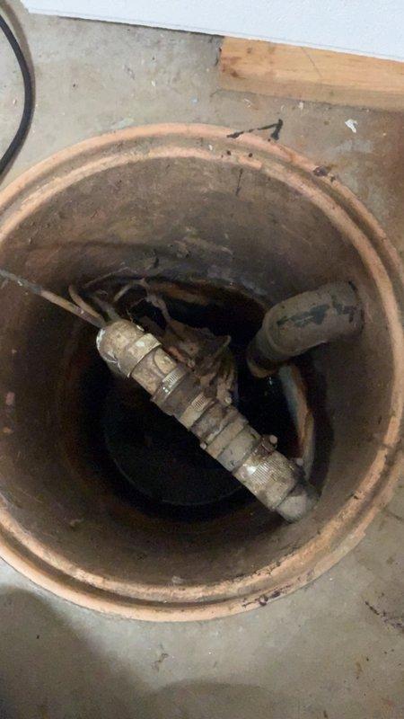 Conducted on-site assessment for sump pump replacement in residential basement. Inspected existing sump pump basin and observed significant deterioration of the clay tile crock with heavy sediment buildup and corroded discharge piping. Evaluated the condition of the pump assembly, noting aged metal fittings, compromised wiring, and substantial corrosion throughout the system. Documented current installation with photographs showing the degraded interior pipe walls, worn threading on connections, and accumulated debris within the basin. Provided comprehensive estimate for complete sump pump system replacement including new basin, pump unit, check valve, and discharge piping to ensure reliable water removal and prevent future basement flooding.