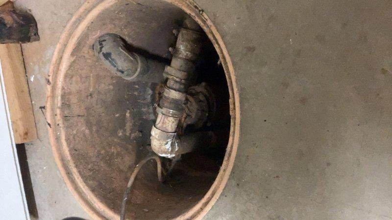 Conducted on-site assessment for sump pump replacement in residential basement. Inspected existing sump pump basin and observed significant deterioration of the clay tile crock with heavy sediment buildup and corroded discharge piping. Evaluated the condition of the pump assembly, noting aged metal fittings, compromised wiring, and substantial corrosion throughout the system. Documented current installation with photographs showing the degraded interior pipe walls, worn threading on connections, and accumulated debris within the basin. Provided comprehensive estimate for complete sump pump system replacement including new basin, pump unit, check valve, and discharge piping to ensure reliable water removal and prevent future basement flooding.