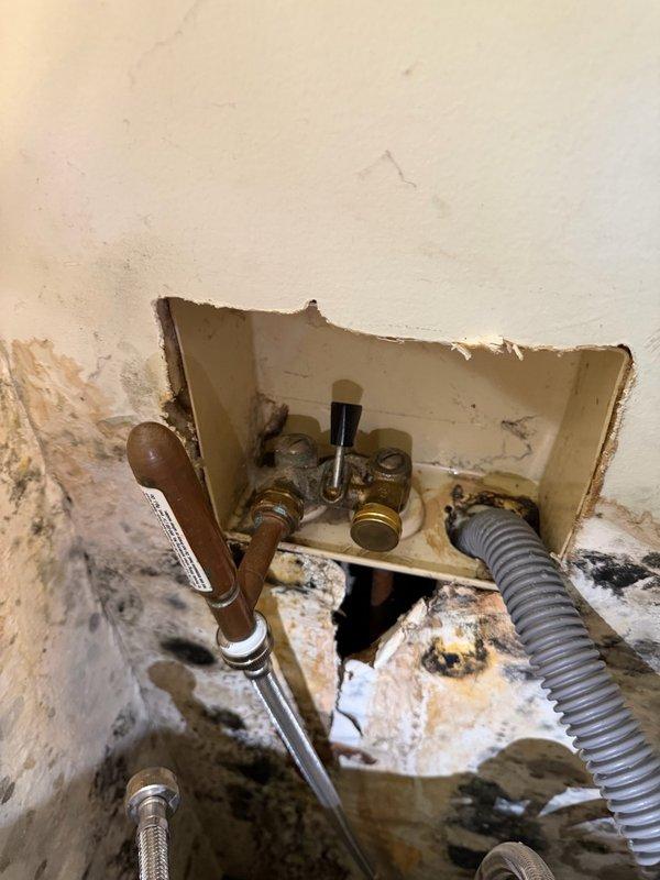 Responded to a water leak emergency in the laundry room where a washing machine supply line was missing a washer, resulting in significant water damage behind the appliance. Shut off the washing machine isolation valves and installed two caps on the supply line outlets to secure the water connections. Coordinated with water damage restoration contractor who will be handling drywall removal and remediation of the affected areas.