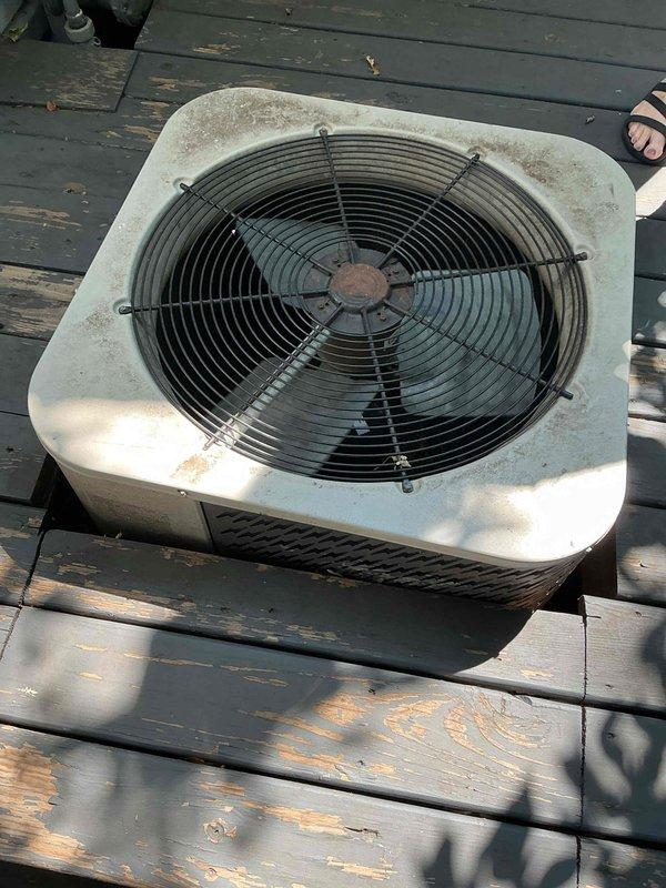 Arrived on-site to perform scheduled AC maintenance on a 20+ year old system. Upon inspection, found the outdoor condenser unit had a deck constructed around it, preventing access to service panels due to stripped screws and structural interference. Unable to proceed with standard maintenance procedures without risk of damaging customer property. Documented equipment condition with photos showing visible dirt accumulation and weathering on the unit exterior. Recommended coordination with comfort advisor and handyman to safely disassemble deck sections for proper system access before maintenance can be completed.