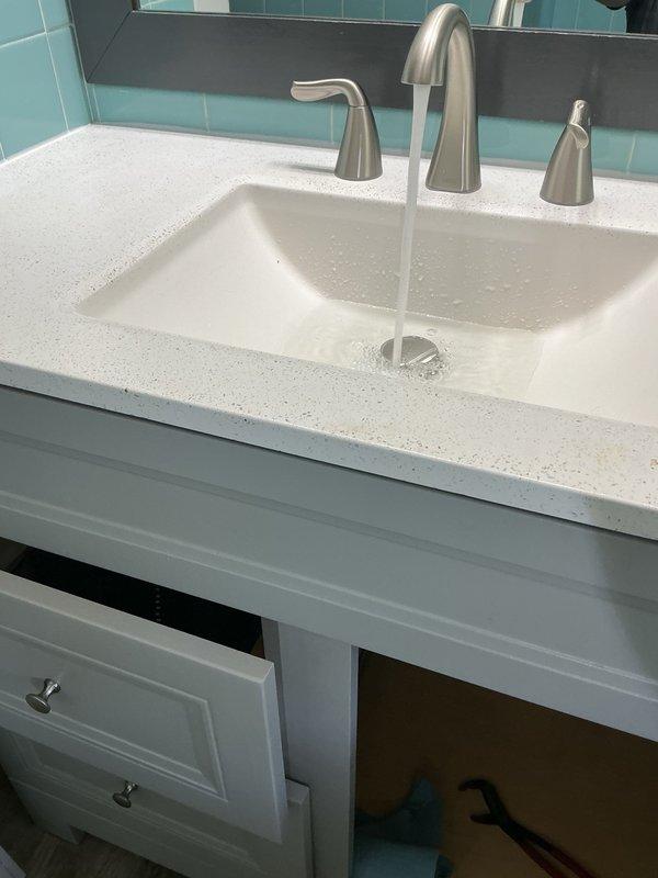 Removed existing bathroom vanity faucet and installed customer-supplied widespread faucet with brushed nickel finish on white solid surface countertop. Connected new three-piece faucet assembly to existing supply lines and shut-off valves. Installed new drain assembly and P-trap configuration, ensuring proper alignment and leak-free connections. Tested water flow through both hot and cold handles, verified drainage function, and confirmed all plumbing connections were secure with no leaks detected.