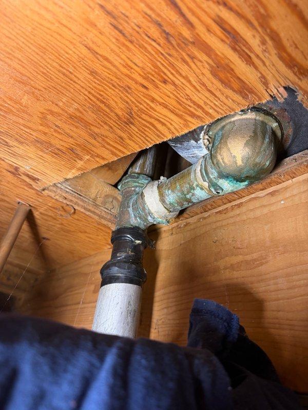 Completed comprehensive plumbing inspection of residential property with focus on aging water supply lines and drain systems. Documented extensive corrosion on vertical black iron drain pipe assembly and copper supply lines in utility area, noting visible rust on metal fittings and deterioration at connection points. Identified corroded trap assembly beneath floor with significant green patina indicating advanced oxidation of brass/copper components, along with evidence of moisture exposure and water staining on surrounding wood subflooring at pipe penetration points. Mixed plumbing materials observed throughout system including older metal components and newer white PVC sections connected via adapters, suggesting previous repair attempts. Provided detailed photographic documentation of all corroded components, leaking water lines, and areas requiring immediate attention. Prepared comprehensive estimate for necessary repairs to address active water line leaks and recommend replacement 