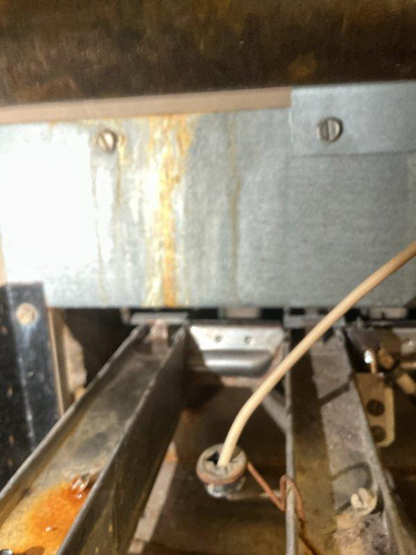 Responded to service call for water intrusion into furnace during rain events. Upon inspection, identified damaged or missing vent cap on furnace flue stack allowing water penetration through vent system. Documented extensive rust staining and corrosion on furnace components, including blower housing panel and internal framework, indicating ongoing moisture exposure. Photographed water damage patterns and deteriorated metal surfaces throughout unit. Recommended roofing contractor for vent cap repair or replacement to resolve water infiltration issue at source.