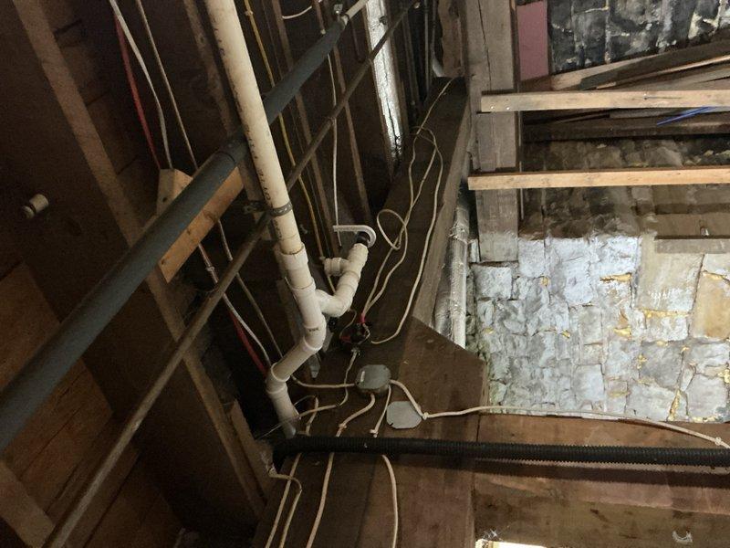 Conducted comprehensive site assessment of duplex property focusing on basement utility infrastructure and existing plumbing systems. Evaluated basement area for feasibility of adding washer/dryer hookups, inspecting existing water supply lines, drainage capabilities, and structural considerations for new appliance installation. Assessed current sump pump system and identified requirements for replacement or upgrade to ensure proper basement water management. Documented existing electrical panel capacity and evaluated garage location for potential 200-amp service upgrade with subpanel installation to support additional electrical loads. Photographed exposed plumbing infrastructure including PVC drainage lines, water supply piping, and existing utility routing through floor joists and wall framing. Noted deteriorated conditions in basement including water-damaged structural elements, aging pipes, and multiple layers of previous modifications requiring consideration during renovation pla
