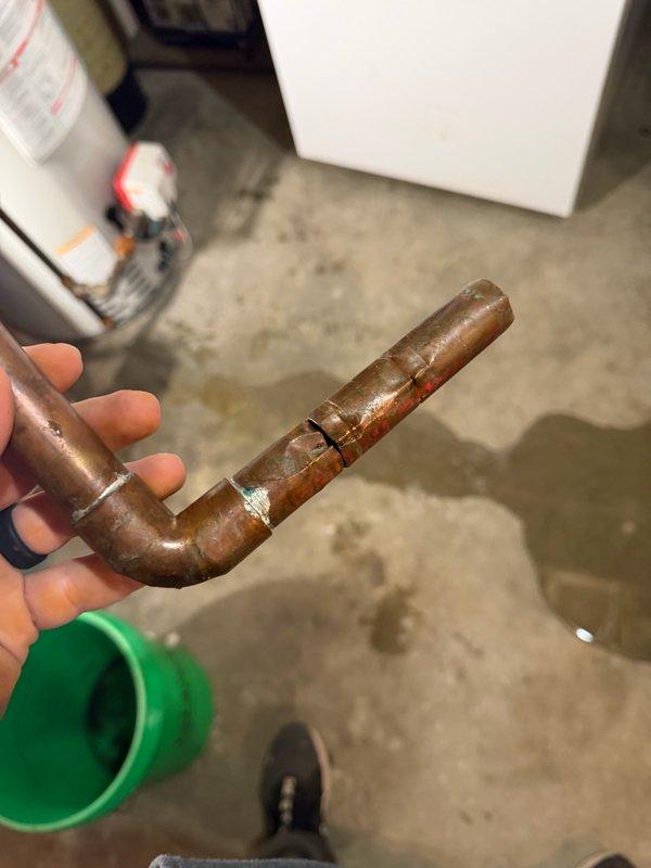 Responded to emergency water leak in mechanical room where a cracked copper pipe feeding the acid neutralizer caused basement flooding. Homeowner had shut off well pump to prevent further water damage upon our arrival. Removed and replaced the corroded section of copper piping, including installation of a new 90-degree elbow fitting to restore water flow to the acid neutralizer system. Water service was successfully restored to the home, and provided estimate for complete acid neutralizer replacement and comprehensive water system repiping due to visible corrosion throughout existing plumbing infrastructure.