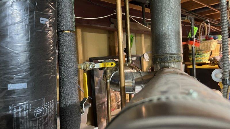 Responded to service call for tanked water heater with multiple concerns including corroded hot water outlet pipe, improperly sloped exhaust venting, and natural gas leaks at appliance connections. Performed comprehensive gas leak search and inspection of the water heater system. Identified exhaust vent pipe sloping downward instead of required upward pitch, creating potential for improper draft and condensation issues. Confirmed corrosion present on hot water outlet piping requiring attention. Located gas leaks at valve connections serving both the clothes dryer and boiler appliances. Documented conditions with photographic evidence showing aged galvanized venting, copper supply piping, and gas line connections throughout the mechanical space. Provided customer with detailed assessment comparing repair options versus full system replacement, outlining benefits and considerations for each approach given the multiple issues identified and overall age of the installation.