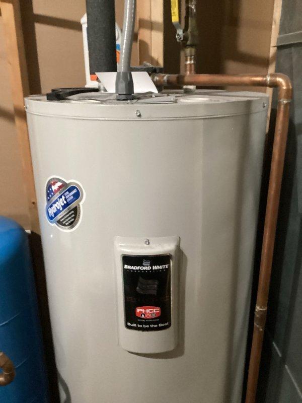 Responded to mystery water leak in basement utility area where pressure tank, furnace, and water heater are installed in close proximity. Upon investigation, identified the Bradford White water heater as the source of the leak, with water dripping from the bottom of the unit. Documented existing equipment condition with photographs showing the conventional tank-style water heater with standard copper and insulated piping connections. Customer requested replacement with tankless water heater system, and service advisor has been notified to schedule the installation.