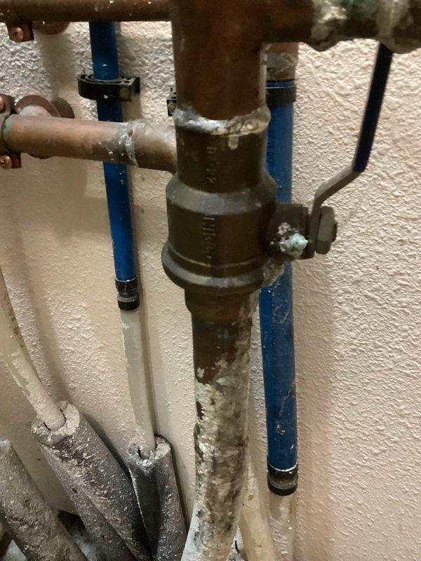 Responded to a mystery water leak in the laundry room and conducted a thorough inspection to identify the source. Located the leak at the main shut-off valve before the meter, which exhibited significant age-related deterioration, corrosion, and patina on the brass valve body. Documented the condition of the aging plumbing assembly with photographs and provided an estimate for main valve replacement, advising that city water shut-off coordination will be required to complete the repair work.