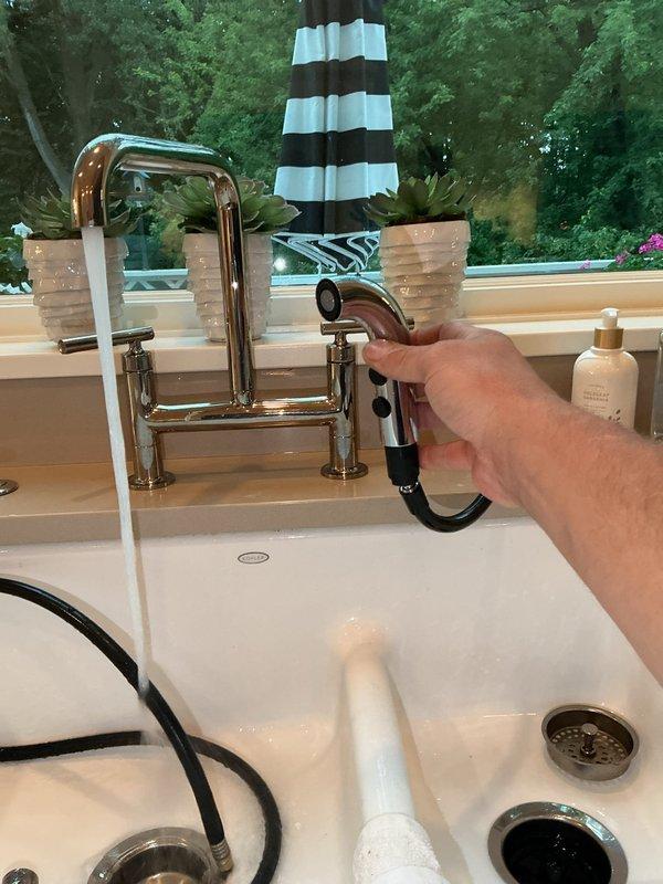 Supplied and installed new kitchen faucet sprayer assembly including chrome spray nozzle with black rubber grip, flexible black hose, and all necessary connections on existing bridge-style kitchen faucet. Verified proper operation of pull-out spray function and checked for leaks at all connection points. Installation includes 1-year parts and labor warranty coverage.