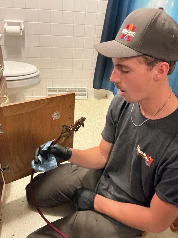 Responded to a plugged bathroom sink drain issue. Upon arrival, disassembled the P-trap and drain piping beneath the vanity to access the blockage. The drain line was severely clogged with debris. Cleared the obstruction using a small rigid snake machine, ensuring proper flow was restored throughout the drain system. Reassembled and reconnected all piping components beneath the sink, including the P-trap assembly and tailpiece connections. Verified all connections were secure with no leaks and confirmed proper drainage function before completing the service.