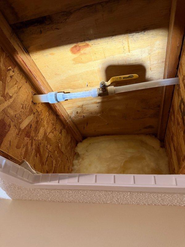 Replaced exterior hose bib with new fixture mounted on white panel against building siding, utilizing copper connections. Installed access panel in basement floor opening to provide future serviceability to the water supply line, which includes PVC piping with shut-off valve and proper insulation at the floor level.