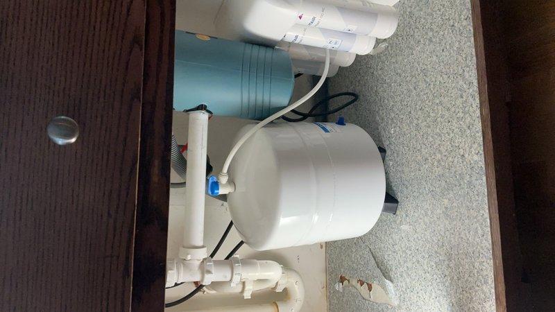 Responded to callback for water leak originating from kitchen sink area and dripping through basement ceiling. Upon inspection, discovered the reverse osmosis system drain line had disconnected from the standpipe beneath the kitchen sink, causing water to overflow and leak through the floor. The drain line likely dislodged due to insufficient insertion depth or pressure from air in the lines during system operation. To prevent future disconnection, drilled a small hole in the standpipe and secured the RO drain line with a zip tie, ensuring permanent attachment. Verified system operation and confirmed no further leakage.