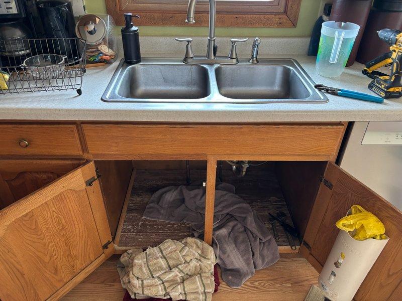 Installed customer-supplied chrome kitchen faucet with dual handles and side sprayer attachment on double-basin stainless steel sink. Verified proper water flow, tested for leaks, and ensured all connections were secure beneath the sink cabinet.