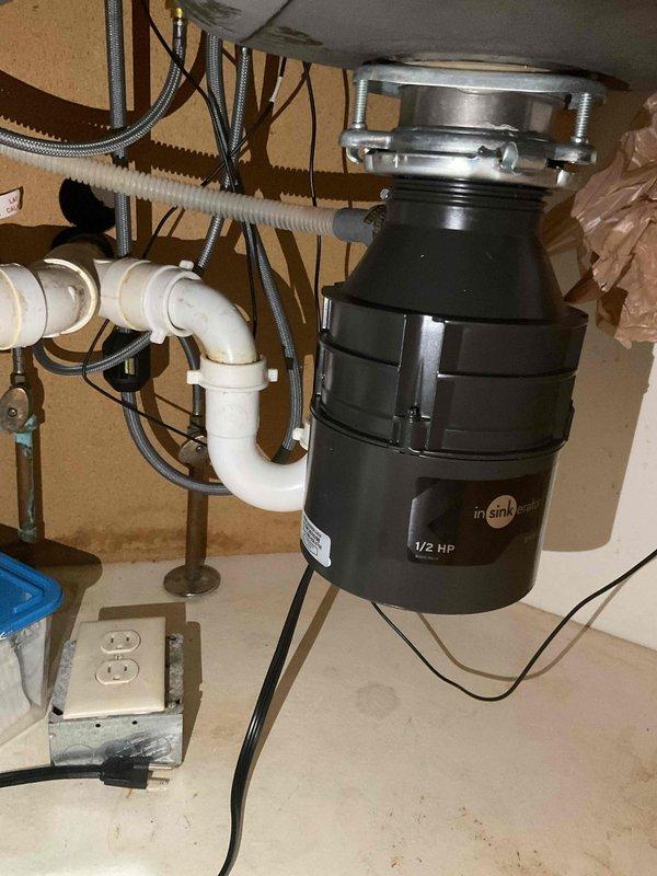 Installed new InSinkErator 1/2 HP garbage disposal unit under kitchen sink, including mounting assembly with stainless steel flange and mounting ring. Connected white PVC drain piping with trap configuration and verified proper electrical connection to existing outlet box with dedicated power cord.