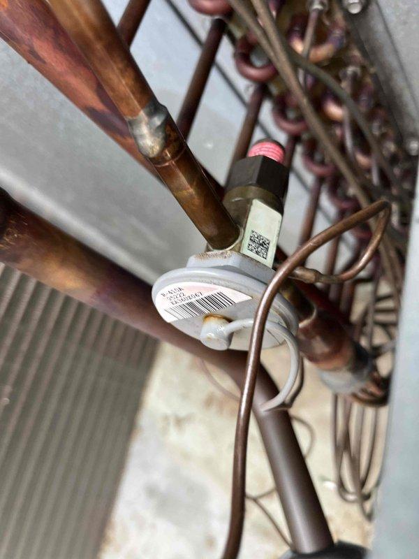 Responded to callback for kitchen AC unit not cooling following previous leak repair. Upon inspection, discovered the small TXV line connecting to the suction line had failed and blown off. Failure attributed to embrittlement of the line from previous brazing repair on the suction line crack, causing the line to become too brittle to withstand system pressure. 

Implemented temporary solution by disconnecting the affected compressor and bypassing its low pressure switch to restore partial cooling capacity with the remaining compressor. This allows the unit to provide cooling while scheduling the permanent repair. 

Full repair will require approximately four hours and involves either reconnecting the TXV line properly or upgrading the TXV assembly to eliminate the need for brazing the small diameter line. Photos documented the failed connection point and affected components. Unit currently operational with single compressor configuration pending scheduled repair completion.