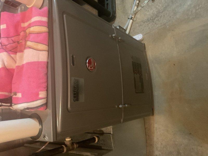 Completed annual cooling maintenance on residential AC system as part of rewards membership agreement. During inspection, discovered significant long-term condensate intrusion issue on 2015 Rheem furnace originating from combustion air intake piping, causing moisture accumulation in blower compartment affecting blower deck and control board. Previous technician had recommended complete vent re-piping; instead installed Fernco-style drain-enabled fitting on intake pipe with braided drain tube and verified proper drainage function by water testing at outdoor intake. AC system (replaced 2022 or 2024, exact year unconfirmed) showed acceptable performance at time of service with normal operating pressures and 19-20°F temperature split across evaporator coil. However, homeowner reported annual refrigerant loss requiring repeated additions, with previous service company identifying suspected evaporator coil leak. Despite normal readings during current visit, historical refrigerant loss patter