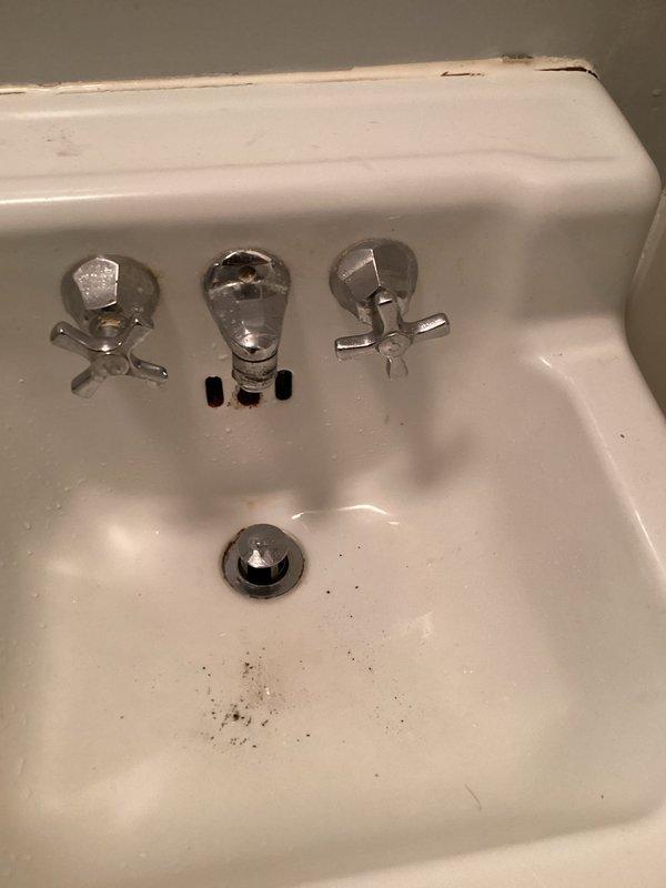 Responded to service call for downstairs bathroom sink with severely reduced water flow. Upon inspection of the white wall-mounted sink with chrome cross-handle faucets, confirmed minimal water output from the faucet. Diagnosed issue as clogged aerator restricting water flow. Removed aerator from faucet spout, cleared debris and sediment buildup, and reinstalled aerator. Tested water flow and verified full pressure restoration to the fixture.