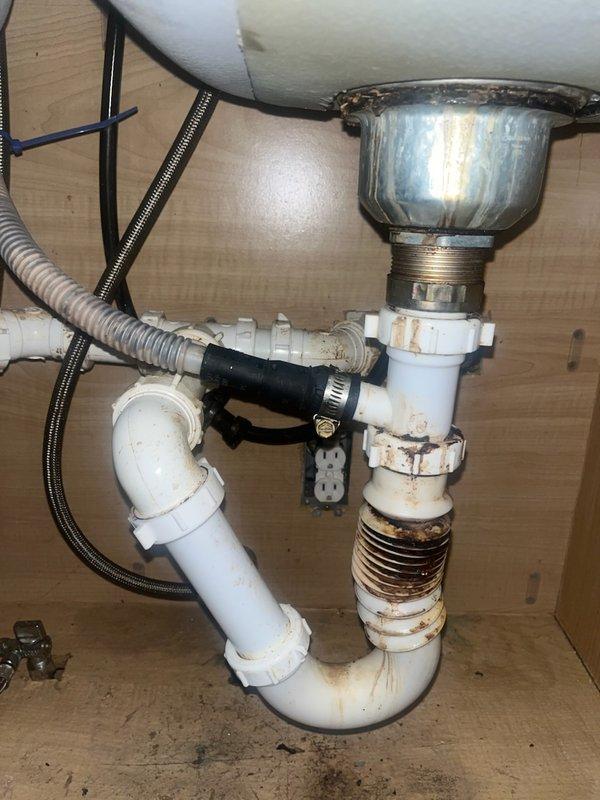 Responded to service call for kitchen sink leak and low water pressure issue in bathroom sink. Upon inspection, identified failed basket strainer assembly with significant corrosion and rust staining at threaded connections under kitchen sink. P-trap and tubular drain assembly showed deterioration with active leaking at multiple connection points. Replaced corroded basket strainer with new chrome unit, installed new PVC P-trap assembly and tubular drain connections. Tested all connections for leaks and verified proper drainage. Inspected bathroom sink faucet with black finish and two-handle configuration for reported low water pressure concern. Isolated issue to aerator blockage, cleaned and reinstalled. Confirmed adequate water pressure restored to bathroom faucet. All plumbing connections secured and leak-free upon completion.