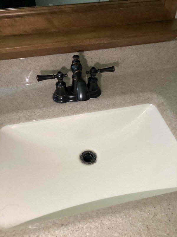 Responded to service call for kitchen sink leak and low water pressure issue in bathroom sink. Upon inspection, identified failed basket strainer assembly with significant corrosion and rust staining at threaded connections under kitchen sink. P-trap and tubular drain assembly showed deterioration with active leaking at multiple connection points. Replaced corroded basket strainer with new chrome unit, installed new PVC P-trap assembly and tubular drain connections. Tested all connections for leaks and verified proper drainage. Inspected bathroom sink faucet with black finish and two-handle configuration for reported low water pressure concern. Isolated issue to aerator blockage, cleaned and reinstalled. Confirmed adequate water pressure restored to bathroom faucet. All plumbing connections secured and leak-free upon completion.