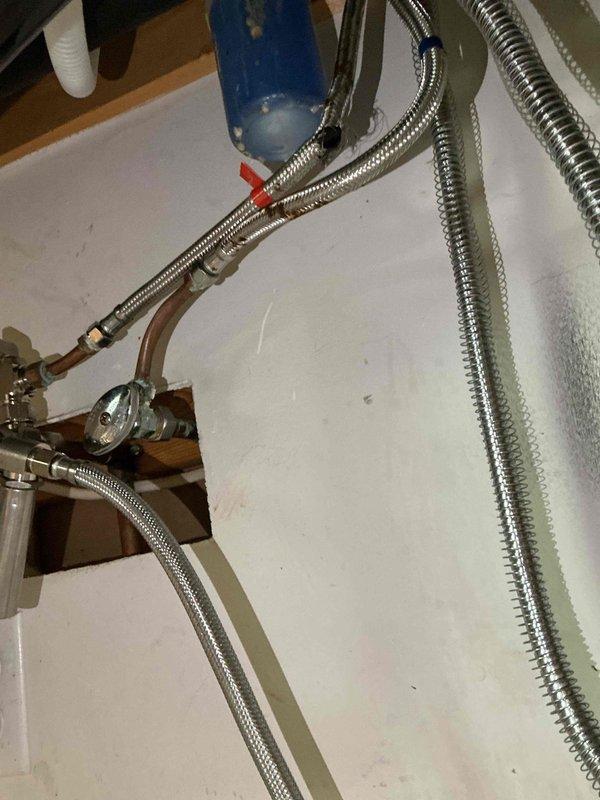 Responded to water leak under kitchen sink caused by burst hot water supply line. Upon inspection, found ruptured flexible braided hose connecting to kitchen fixture had failed, resulting in water damage to ceiling below. Shut off water supply at isolation valve and removed damaged flex line. Installed customer-provided replacement braided stainless steel flex hose to hot water line, ensuring proper connection to copper piping and fixture supply. Tested system for leaks, verified water flow, and confirmed repair integrity. Documented existing plumbing configuration and water heater installation in basement area showing signs of previous moisture exposure on flooring.