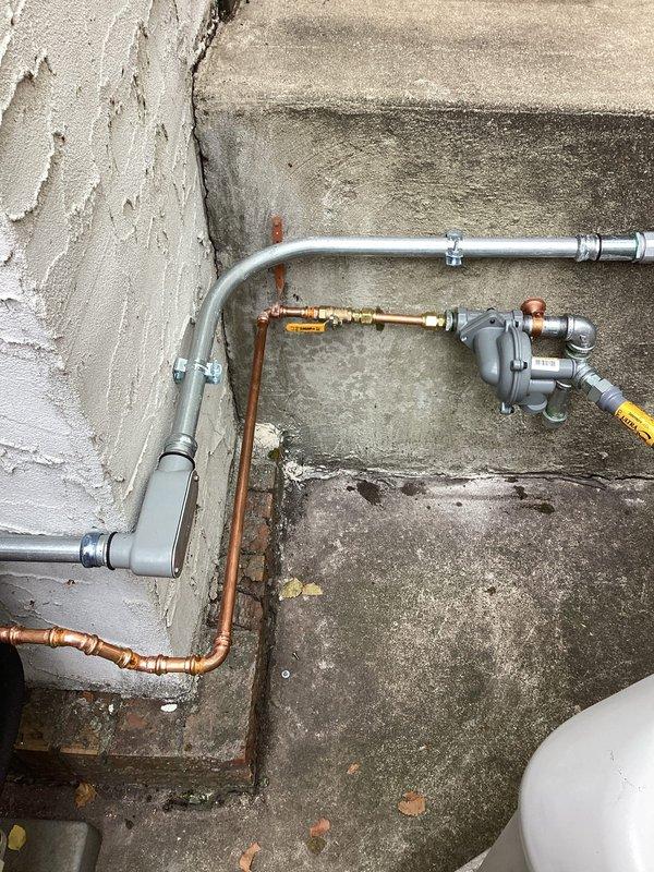 Completed callback to correct gas piping installation to residential generator. Removed and replaced non-compliant black iron piping with code-approved materials, installed new gas regulator in improved location for proper clearances and accessibility, and replaced existing gas whip with correct specification flexible connector. Repositioned gas meter assembly and modified piping configuration to meet current code requirements, ensuring proper support and routing of all gas lines from meter to generator unit.