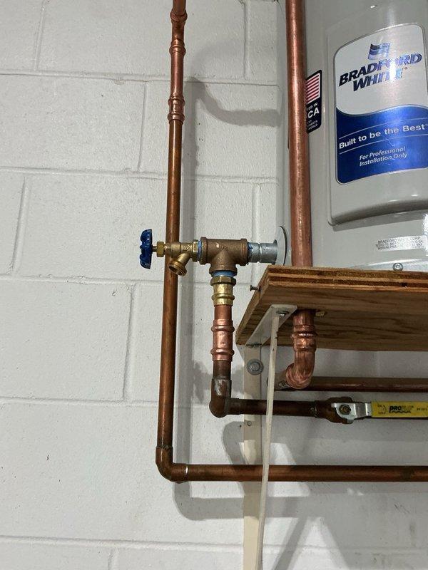 Removed and disposed of existing failed water heater. Supplied and installed new 12-gallon Bradford White water heater on wall-mounted wooden platform. Connected copper supply lines with brass fittings and installed blue-handled ball valve for system shut-off control. Reconnected temperature and pressure relief valve and added new drain line to unit, as previous installation lacked proper drainage. Set thermostat to match previous unit's temperature setting. Installation includes manufacturer warranty and 1-year parts and labor warranty. System tested and operational upon completion.