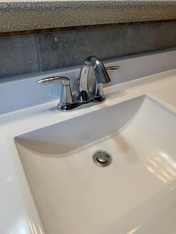 Responded to service call for loose bathroom faucet handle on chrome two-handle centerset faucet assembly. Upon inspection, determined that the handle had become unspun from its mounting base, causing it to detach during normal operation. Tightened and secured the faucet handle back onto the valve stem, restoring proper function and stability to the fixture.