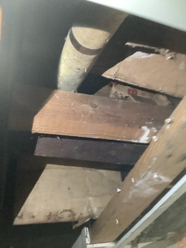Responded to service call for boiler system with frozen and damaged hydronic heating piping. Upon inspection, found severely corroded 1" black iron pipe with perforation and breach in inaccessible location serving baseboard heating loop in rear section of main level. Corrosion and freeze damage resulted from loop being shut off during previous winter season. Provided estimate for repair solution involving isolation of damaged section by installing shut-off ball valves at accessible basement location, abandoning deteriorated black iron piping in place, and running new PEX tubing to supply side of existing baseboard units. Main boiler system confirmed operational and serving remaining radiators throughout property. Documented existing conditions with photographs showing extent of pipe corrosion, perforation damage, and confined crawl space access constraints.