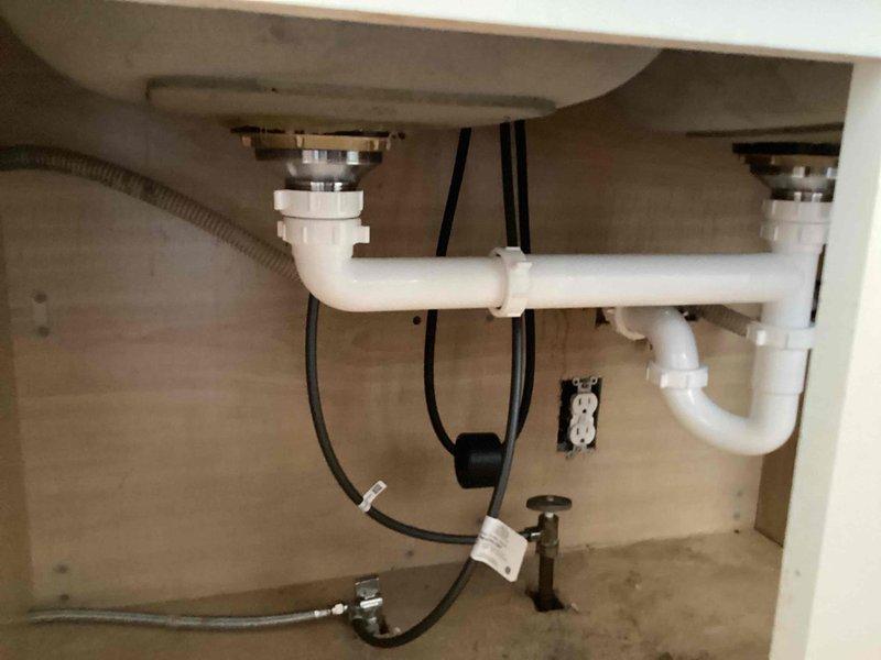 Completed installation of dual basket strainers with kitchen sink repiping and customer-supplied faucet installation. Replaced existing drain assembly with new chrome basket strainers, installed white PVC P-trap configuration with proper compression fittings, and connected dishwasher drain line to disposal knockout. Installed new shut-off valves for hot and cold water supply lines and completed all connections to ensure proper drainage and water flow. All plumbing components were tested for leaks and verified operational upon completion.