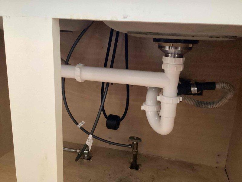 Completed installation of dual basket strainers with kitchen sink repiping and customer-supplied faucet installation. Replaced existing drain assembly with new chrome basket strainers, installed white PVC P-trap configuration with proper compression fittings, and connected dishwasher drain line to disposal knockout. Installed new shut-off valves for hot and cold water supply lines and completed all connections to ensure proper drainage and water flow. All plumbing components were tested for leaks and verified operational upon completion.