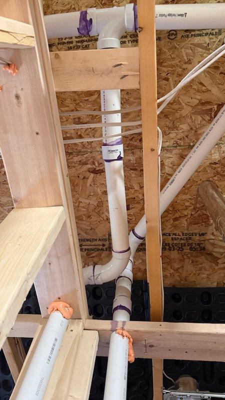 Responded to service call for reported bathroom exhaust fan ductwork leaking in attic space during home remodeling. Upon inspection of the attic area with rafters at 9 feet high and pipes approximately 10 feet from floor, determined that the issue was not HVAC-related ductwork but rather plumbing drainage system. Identified multiple 2" and 3" PVC couplings and fittings installed by homeowner that were causing slow water leaks in the vertical drain/vent piping system. Documented conditions with photographs showing PVC pipe assembly with couplings, T-joints, and purple pipe hangers secured to wooden framing in exposed construction area. Informed office that plumbing specialist would be required to address the leaking PVC connections, but no plumbers were available for immediate dispatch through the weekend.