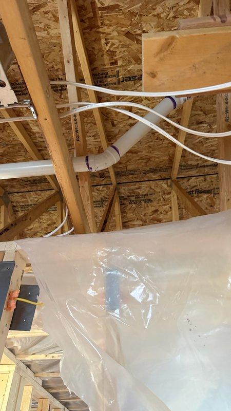 Responded to service call for reported bathroom exhaust fan ductwork leaking in attic space during home remodeling. Upon inspection of the attic area with rafters at 9 feet high and pipes approximately 10 feet from floor, determined that the issue was not HVAC-related ductwork but rather plumbing drainage system. Identified multiple 2" and 3" PVC couplings and fittings installed by homeowner that were causing slow water leaks in the vertical drain/vent piping system. Documented conditions with photographs showing PVC pipe assembly with couplings, T-joints, and purple pipe hangers secured to wooden framing in exposed construction area. Informed office that plumbing specialist would be required to address the leaking PVC connections, but no plumbers were available for immediate dispatch through the weekend.