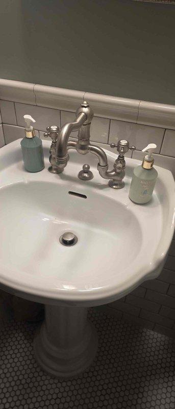 Responded to service call for two bathroom faucet issues including one leaking faucet and one leaking connection with no hot water supply. Inspected white pedestal sink with brushed nickel two-handle faucet fixture and identified water leak requiring repair. Assessed both faucet assemblies, diagnosed necessary repairs, and documented conditions with photographs. Provided estimates for required parts and arranged for ordering of components needed to complete repairs.