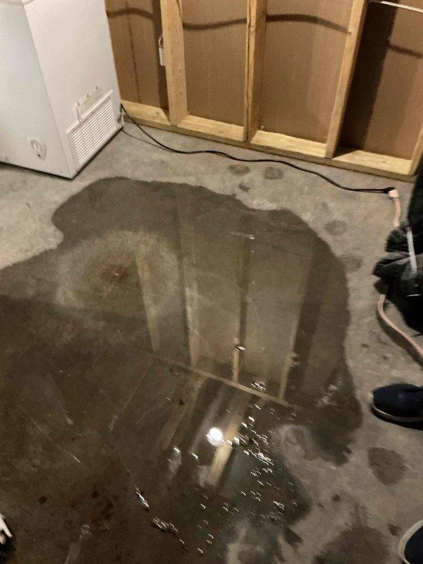 Responded to a no cooling call and member tune-up request for a 5-year-old natural gas furnace system. Upon arrival, discovered extensive water pooling around the furnace and on the concrete floor of the mechanical space. Diagnosed that water leakage occurred only when the HVAC system was operational and ceased when the unit was turned off, indicating a condensate drainage issue rather than an equipment malfunction. Inspected the condensate drain system and confirmed that the drain line was completely plugged, causing water to back up and overflow around the furnace base. No error codes were present on the unit at time of inspection. Documented the water damage with photographs showing standing water on the floor and moisture staining on the concrete surface. Coordinated with dispatch to schedule a specialized drains technician to clear the blocked condensate line and restore proper drainage function.