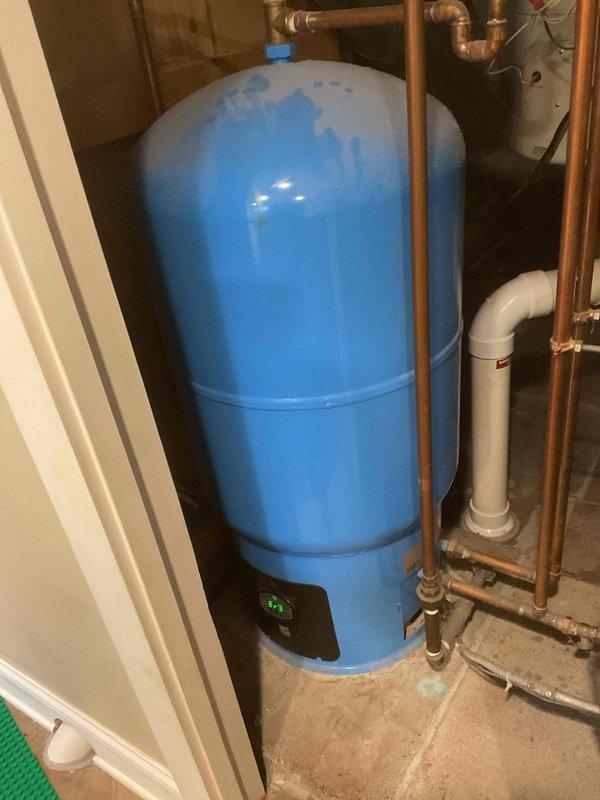 Responded to no hot water complaint and investigated 12-5 water heater displaying Error Code 3. Upon arrival, found Amtrol DX-69 pressure tank system with aged equipment that had been in service for over six years. Inspected the blue pressure expansion tank, associated copper piping connections, and digital control unit. During diagnostic evaluation, identified boiler system with critically low pressure affecting overall hot water production. Assessed the mechanical room containing teal-colored boiler unit with extensive black iron piping network, circulation pump, and multiple zone valves. Documented equipment conditions through photographs showing pressure tank installation, boiler configuration, and interconnected plumbing systems including copper and PVC components. Referred boiler pressure issue to HVAC department for proper system pressurization and further evaluation of heating system functionality, as the low boiler pressure was determined to be the root cause affecting hot wat